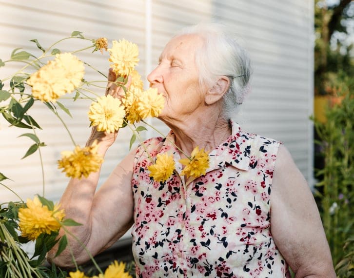 sunlight shining on older woman smelling flowers